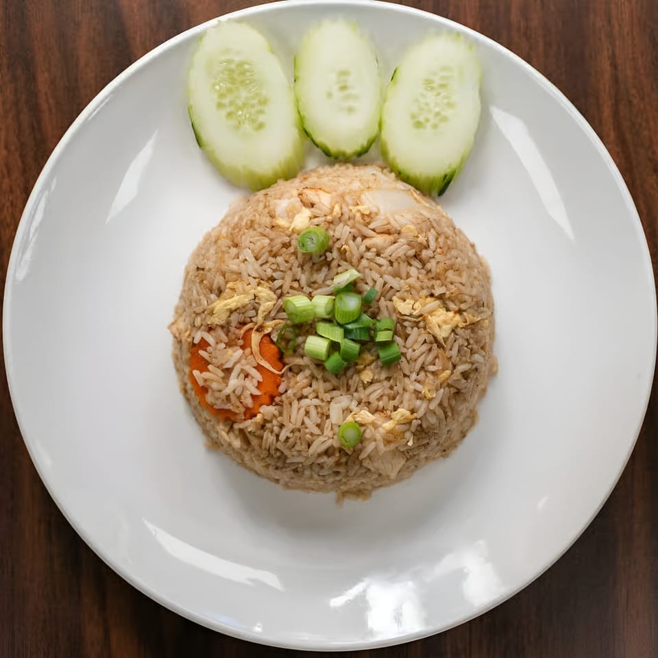 Fried rice with chopped green onions, carrots, and scrambled egg, served with three cucumber slices.
