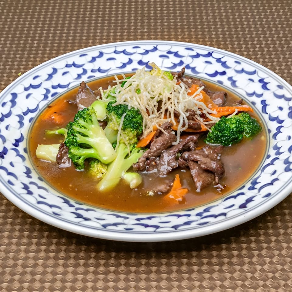 Beef and broccoli stir-fry with carrots and crispy noodles in a brown sauce on a decorative plate.
